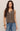 Woman wearing a brown sleeveless button-up shirt and blue jeans against a beige background
