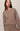 A woman wearing a taupe-brown crewneck knit sweater and matching knit bottoms, photographed against a plain light beige studio background.