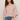 Woman wearing a light pink blouse and blue jeans against a plain background