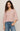 Woman wearing a light pink blouse and blue jeans against a plain background
