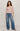 Woman wearing a pink cardigan and blue jeans on a plain background