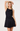 A blonde model wearing a black satin-like halter mini dress with gold hardware accents on the shoulder straps, posed against a clean white studio background.