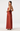 A woman modeling a rust-colored satin halter maxi dress with an open back and side tie, shown from the back against a light gray studio background.
