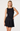 A blonde model wearing a sleeveless black satin mini dress with gold shoulder embellishments, photographed against a clean white studio background.